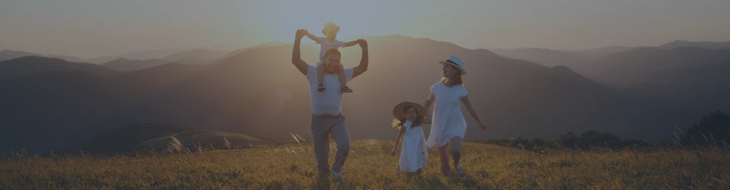 A family of four in a grassy field with mountains in the background.