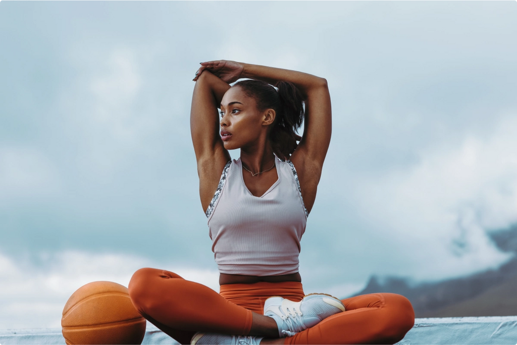 A woman doing stretches outside next to a basketball.