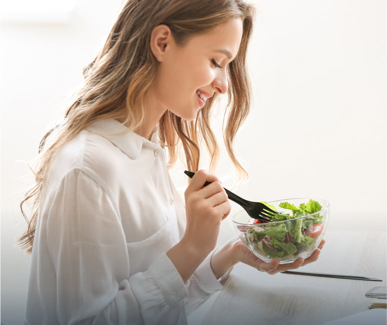 A young woman in a white shirt eating a bowl of salad.
