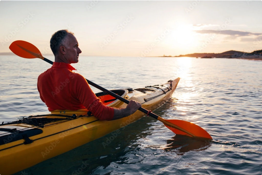 A man paddling a kayak on a lake at sunset.