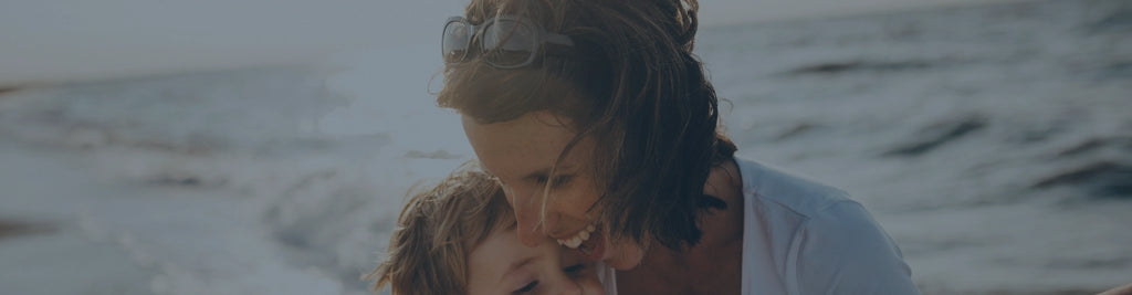 A woman on the beach smiling and hugging a child.