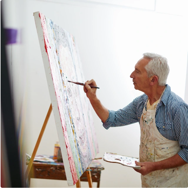 A man with white hair painting on a large canvas.