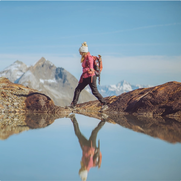 A woman hiking over a river with mountains in the background.