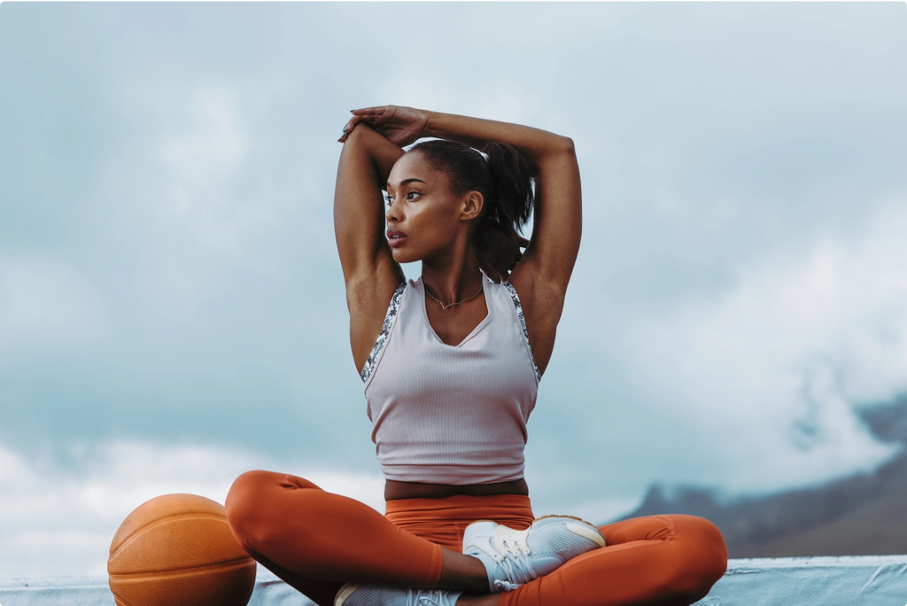 A woman outside doing stretches next to a basketball.