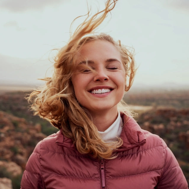 A woman outside smiling at the camera while her hair blows in the wind.