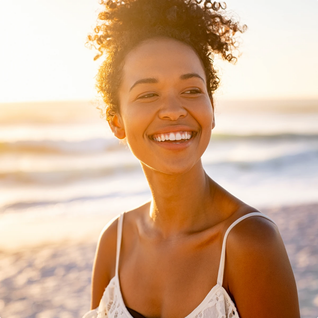 A woman on the beach at sunset smiling toward the camera.