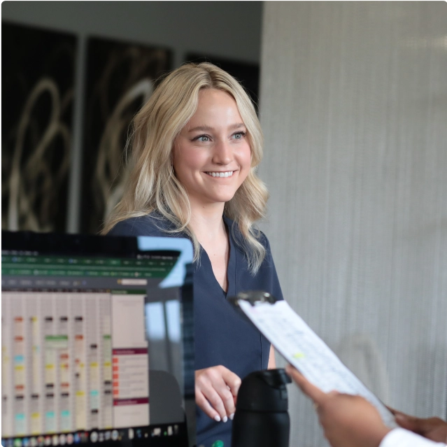 A receptionist smiling and talking to someone holding a clipboard. 