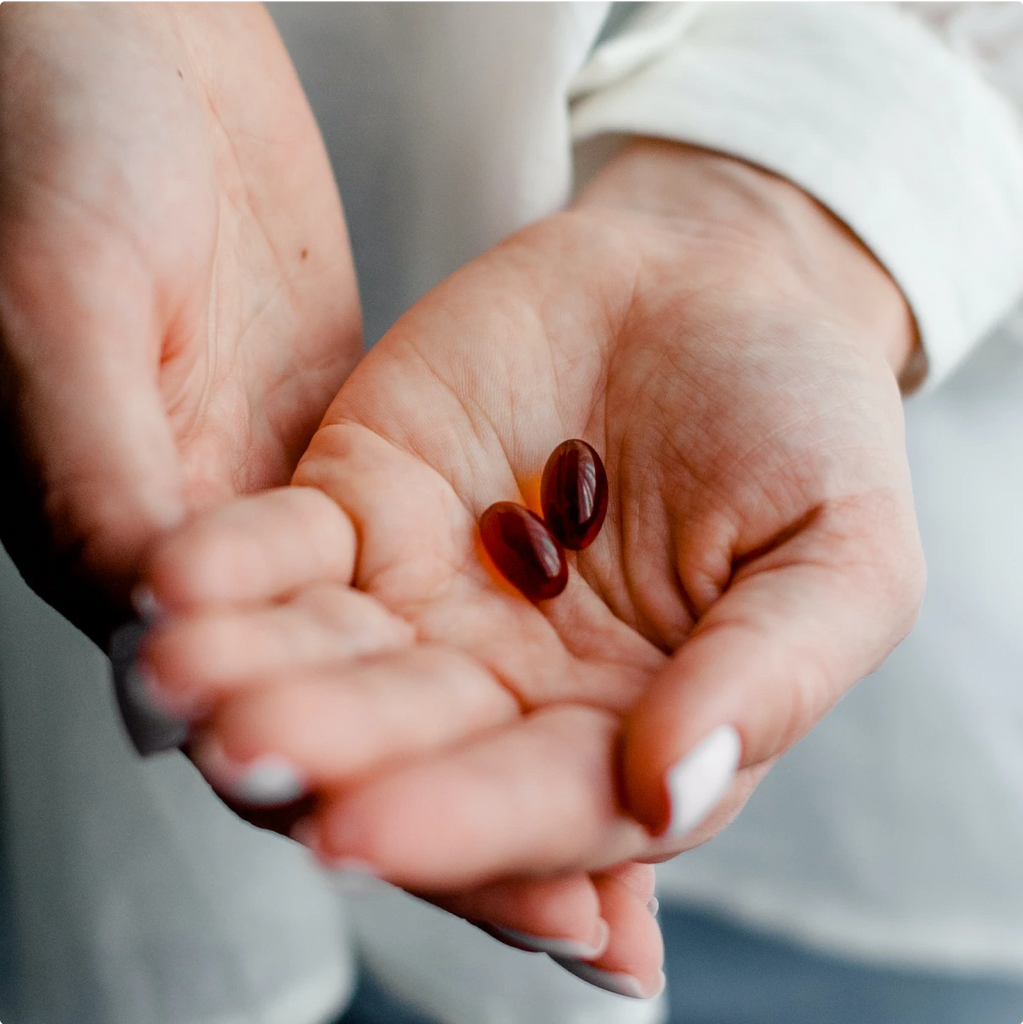 A closeup of a person's hands holding two red gel capsule pills.